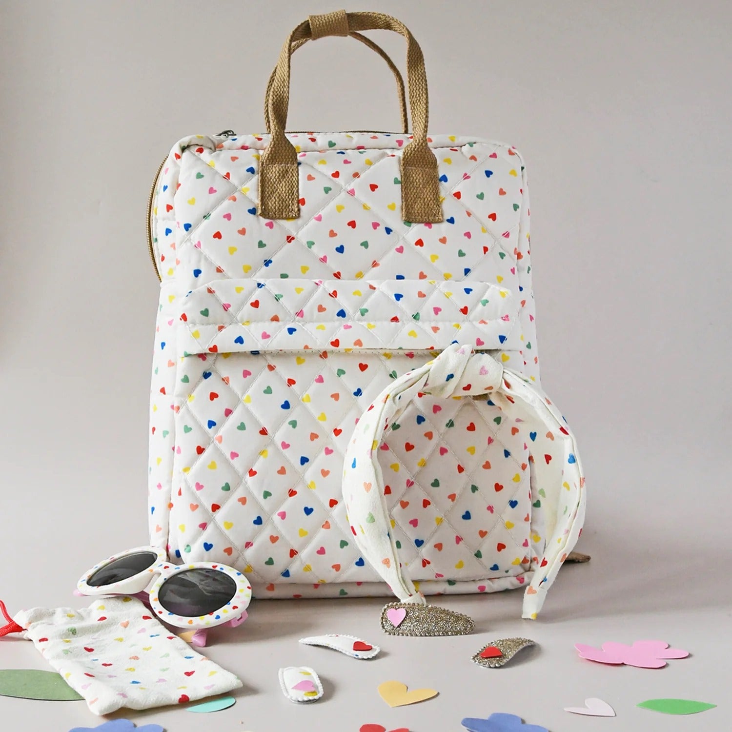 תיק גב מעוצב וכייפי עשוי מבד קווילט בדוגמת לבבות בצבעי הקשת בגודל המושלם לשאת דברים חיוניים ליום יום! תיק גן זה מרופד במלואו עם בד פסים ורודים, הוא כולל כיס קדמי עם רוכסן, ידית נשיאה ורצועות אחוריות מתכווננות. מידות התיק: 30 ס"מ על 24.5 ס"מ על 9 ס"מ.