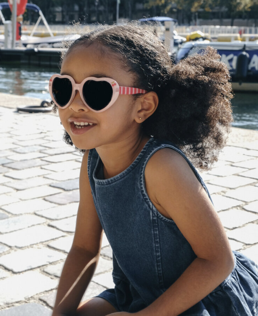 ילדה מתוקה עם משקפי שמש בצורת לב עם עיטור דובדבן. הגנת UV מלאה.