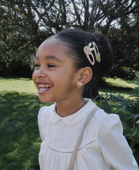 ילדה מחייכת עם עגילי קליפס וסיכות שיער בצורת ארנבת ולב מנצנץ של רוקוהולה קידס