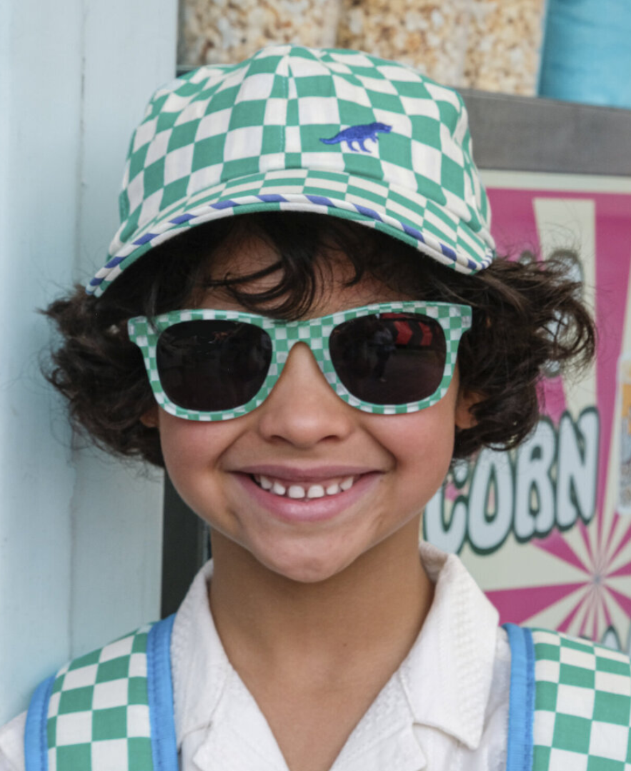 ילד מתוק עם כובע מצחייה קייצי מבד משבצות ירוק ורקמת דינוזאור